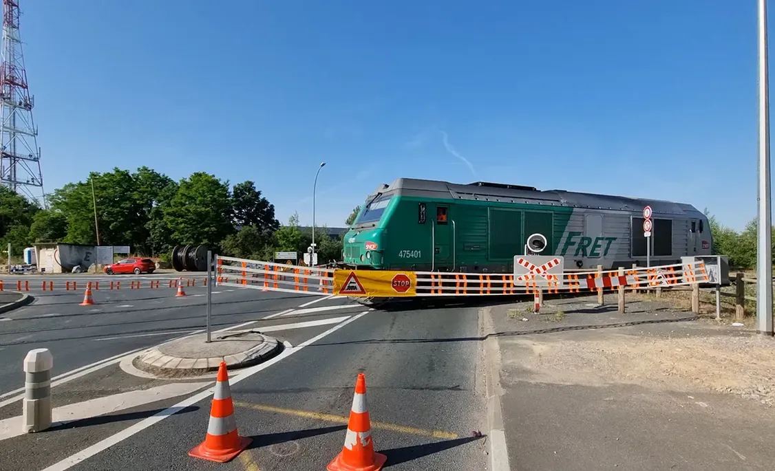 Train de fret passant derrière une barrière textile STOP fermant le passage à niveau