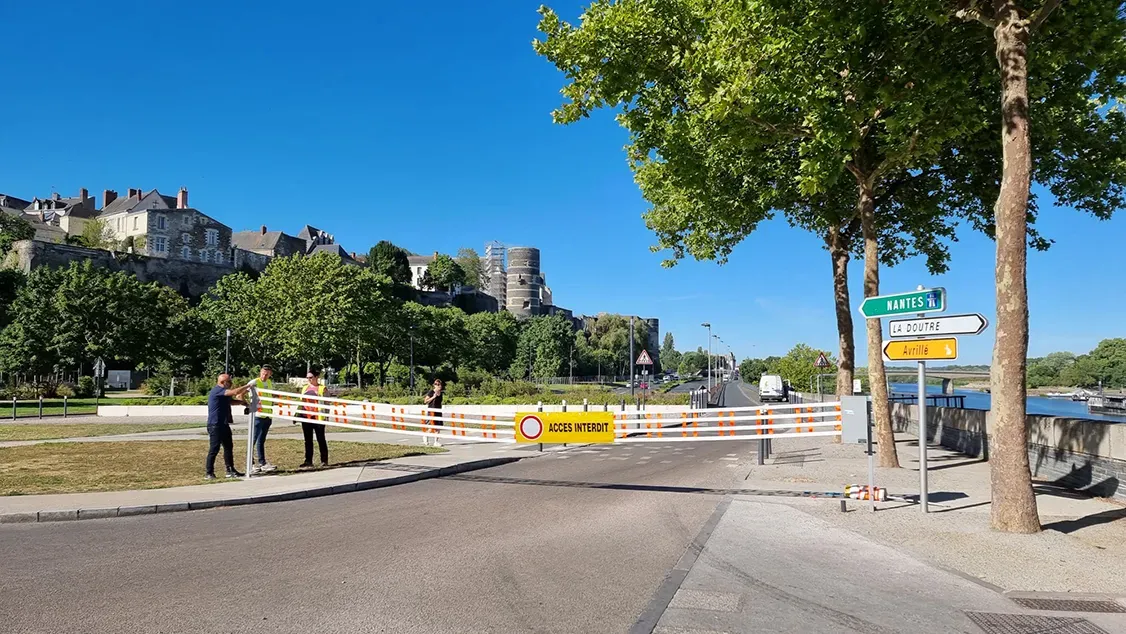 Équipe fermant les voies sur berge d'Angers avec une barrière textile ACCÈS INTERDIT, château en arrière-plan